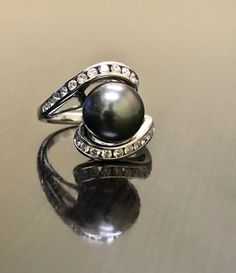 DeKara Designs Collection Beautiful Art Deco/Vintage/Modern Style Pearl Engagement Ring. Metal- 14K White Gold, .583. Stones- 10 MM Round Tahitian/South Sea Black Pearl, 24 Round Diamonds, F-G color SI1-SI2 Clarity, 0.62 Carats. The ring is beautiful with a unique Tahitian pearl that is round in shape. This is a fantastic pearl that is also rare to find. The diamond has two rows of channel set diamonds that are all equivalent in size. The pearl is professionally set in the center of the ring. Si Black Luxury Pearl Ring For Formal Occasions, Black Pearl Formal Ring With Round Shape, Classic Black Pearl Ring For Anniversary, Classic Black Pearl Ring For Wedding, Formal Black Pearl Ring With Round Shape, Black Pearl Ring In Fine Jewelry Style, Classic Black Pearl Ring, Black Pearl Ring Fine Jewelry, Fine Jewelry Black Round Pearl Ring