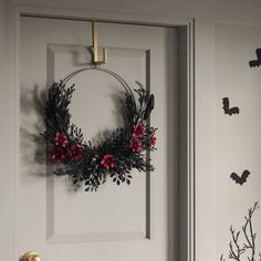 a wreath is hanging on the front door with bats around it and red berries are in the foreground