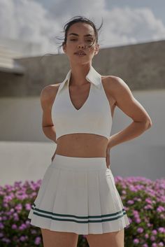 a woman standing in front of flowers wearing a white tennis outfit