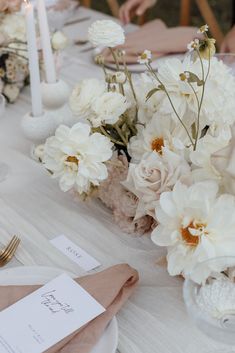 the table is set with white flowers and place cards for guests to sit down at