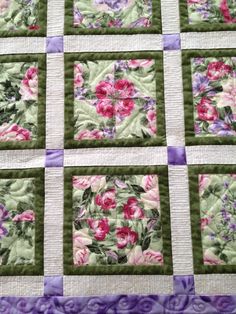 a quilted table topper with pink and purple flowers on green, white and lavender squares