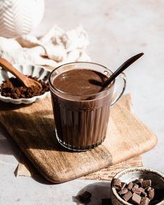 a cup of hot chocolate next to a spoon and bowl of cocoa on a table