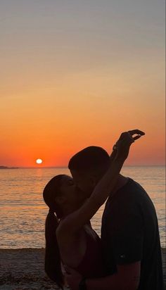 a man and woman are kissing on the beach as the sun sets in the background