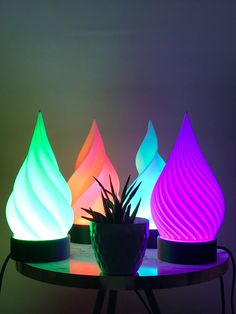 three different colored lights sitting on top of a table next to a potted plant