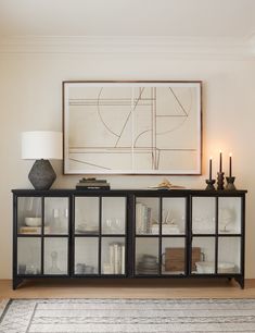 a living room with a large painting on the wall next to a glass cabinet filled with books