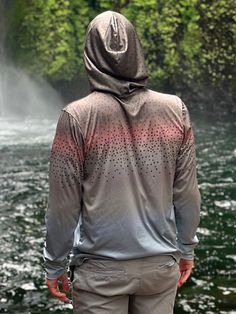 a man standing in front of a waterfall with his back turned to the camera and wearing a hoodie