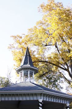 a white gazebo with a clock on it's face in front of trees