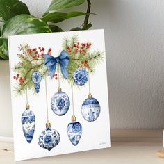 a card with blue and white ornaments hanging from it's sides on a table next to a potted plant