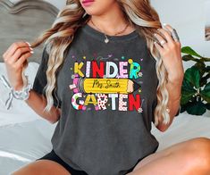 a woman sitting on top of a bed wearing a shirt that says kinder the best caten