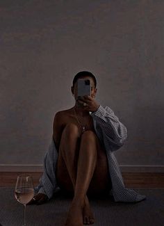 a man sitting on the floor taking a selfie with his cell phone next to a glass of wine