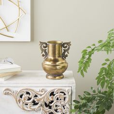 a gold vase sitting on top of a white table next to a potted plant