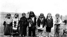 an old black and white photo of children in native american clothing standing on the grass