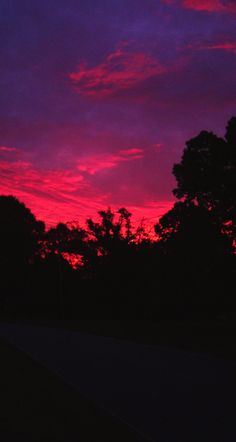 the sky is pink and purple as the sun goes down in the distance behind some trees