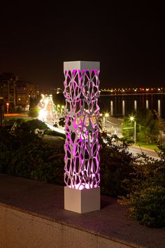 a tall sculpture sitting on top of a sidewalk next to a lush green park at night