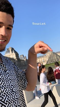 a young man is holding something in one hand and smiling at the camera while people are walking around him