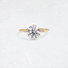 a yellow gold engagement ring with a round brilliant cut diamond in the center, on a white background