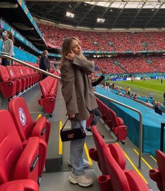 a woman standing in the stands at a soccer game with her cell phone to her ear