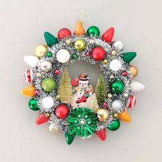 a christmas wreath ornament hanging on a wall with ornaments around it and a snowman in the center