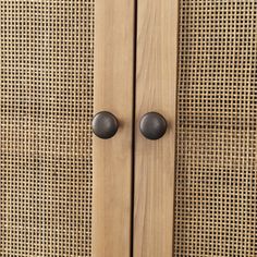 a wooden cabinet with two black knobs on it's sides and a wicker wall behind it