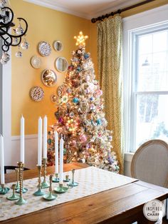 a decorated christmas tree in the corner of a dining room table with candles on it