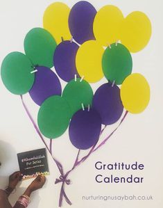 a person holding a book in front of a bunch of balloons with the words gratitude calendar written on it