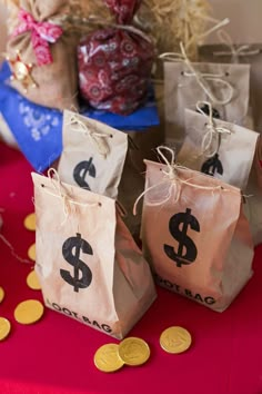 three bags with dollar signs on them are sitting on a red tablecloth next to some gold coins