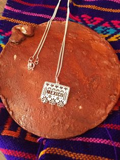 "Beautiful necklace made of 925 silver by artisans from Guerrero, Mexico with a Papel Picado pendant, it is part of our Frida collection available only this month ✨This preorder may take 7 to 15 business days to ship, if you have any questions before ordering send us a message Measurements: 9.5\" length / Papel Picado 1.5 cm CARE: -Do not apply perfume directly -Do not expose to cleaning chemicals -Store in jewelery box" Engraved Pendant Necklace Souvenir, Sterling Silver Pendant Charm Necklace, Sterling Silver Hallmarked Pendant Charm Necklaces, Sterling Silver Hallmarked Pendant Charm Necklace, Silver Pendant Souvenir Jewelry, Silver Pendant Jewelry As Souvenir, Silver Pendant Jewelry For Souvenirs, Silver Charm Necklace With Square Sterling Pendant, Silver Sterling Square Pendant Charm Necklace