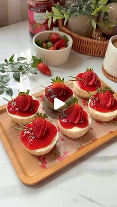 strawberry cheesecakes are arranged on a wooden tray with strawberries in the background