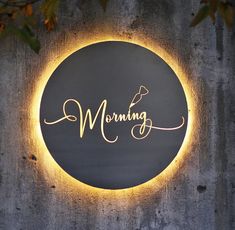 a round sign with the word morning written in cursive gold on a grey wall