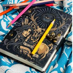 an open notebook with colored pencils next to it on a blue and white blanket