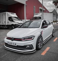 a white volkswagen car parked in front of a red building with two trucks behind it