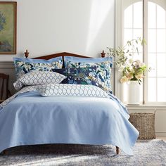 a bed with blue comforter and pillows in a white room next to a window