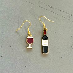 a pair of wine bottle and glass dangle earrings on a gray surface with gold earwires