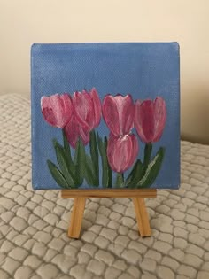 a small easel with pink flowers painted on it sitting on a white bed sheet