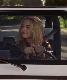 a woman sitting in the driver's seat of a white car with her hand on the steering wheel