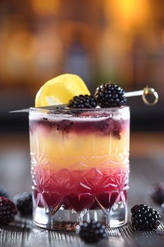 a colorful drink with blackberries and lemon on the rim, sitting on a table