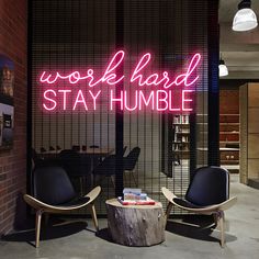 two chairs in front of a neon sign that reads work hard, stay humble