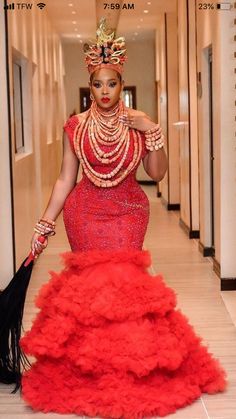 a woman in a red gown and headpiece is walking down the hall with her hand on her hip