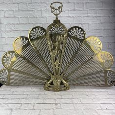 an ornate metal fan with gold accents against a white brick wall in the shape of a peacock