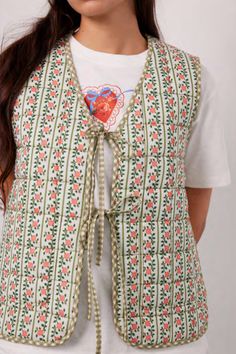 a woman wearing a white shirt and green vest with an orange flower on the front