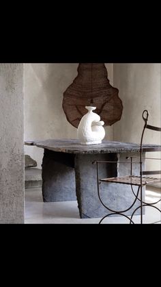 a white vase sitting on top of a table next to a metal chair and wall sculpture