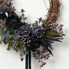 a wreath with purple flowers and greenery hanging on the wall