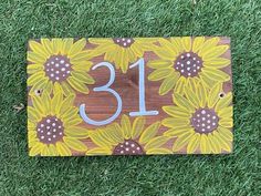 a wooden sign with sunflowers and the number thirteen on it sitting in grass