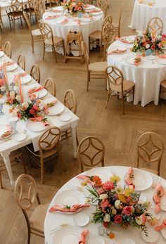 an overhead view of tables and chairs with white tablecloths, orange napkins and floral centerpieces