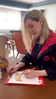 a woman sitting at a table writing on a piece of paper with scissors in front of her