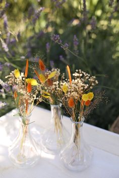 three vases filled with flowers sitting on top of a white table covered in purple and yellow flowers