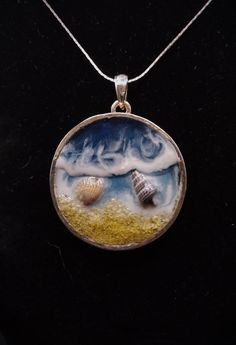 a necklace with two seashells in it on a black background and an ocean scene