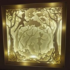 an illuminated shadow box with a silhouette of a fairy on it's face and trees in the background