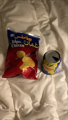 a bag of chips and a can of soda on top of a white bed sheet