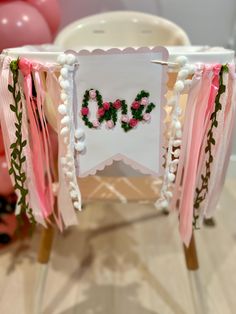 a pink and white decorated chair with flowers on the back is sitting in front of balloons